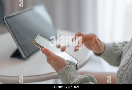 Frau, die von zu Hause aus mit Tablet und Telefon arbeitet. Frau Hände mit Handy. Abgeschnittene Ansicht der Hände einer Frau, die das Mobiltelefon mit Kontakten hält. Verwenden Stockfoto