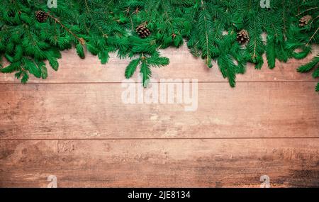 Tannenzweig mit Weihnachtsschmuck auf altem braunem Holzhintergrund mit Platz für Text. Festliche Weihnachtskomposition auf altem Holzhintergrund Stockfoto