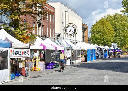 Einkaufen High Street View Straßenrand Marktstände in Brentwood Essex Radfahrer, die entlang Kopfsteinpflaster Straße Uhr falsch Zeit England Großbritannien radeln Stockfoto