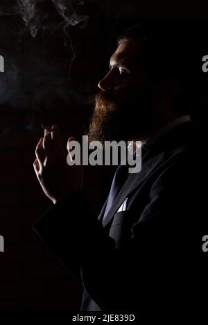 Mann, der Zigarette raucht, isoliert auf Schwarz. Ein Mann raucht Cannabis-Unkraut, ein Gelenk und ein Feuerzeug in seinen Händen. Rauch auf schwarzem Hintergrund. Konzepte von Stockfoto