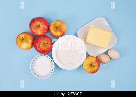 Apfelkuchen Backzutaten mit Butter, Mehl, Zucker, Eiern und Früchten auf blauem Hintergrund Stockfoto