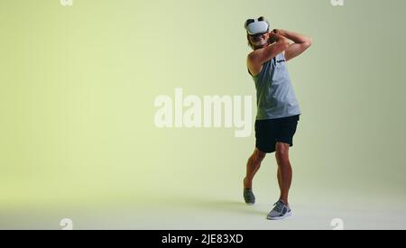 Glücklicher älterer Mann, der lächelt, während er in der virtuellen Realität Golf spielt. Ein reifer Mann, der mit einem Paar Gaming-Controllern einen Golfschwung spielt. Senior Sportler ma Stockfoto