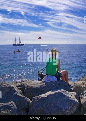 Frau, die auf einem Felsen am Strand sitzt und den Atlantik, Puerto de Mogan, den Kanarischen Inseln, den Kanarischen Inseln, Spanien, Europa Stockfoto