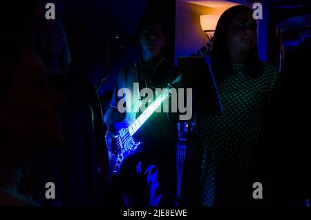 Ein Musiker in der Sub spielt eine Gitarre, die blau und grün beleuchtet wird, bei einem Pub-Auftritt Stockfoto