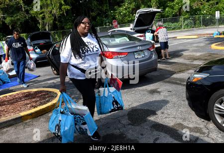 Orlando, Usa. 25.. Juni 2022. Freiwillige laden Beutel mit Lebensmitteln für Bedürftige in Autos bei einer Lebensmittelverteilungsveranstaltung, die von der Second Harvest Food Bank of Central Florida und Orange County in der St. John Vianney Church in Orlando, Florida, gesponsert wird. Hohe Lebensmittel- und Gaspreise drücken die arbeitenden Familien unter Druck und schicken einige zum ersten Mal in Lebensmittelvorratskammern, aber die Anbieter kämpfen mit den Inflationskosten, da die Nachfrage steigt. Kredit: SOPA Images Limited/Alamy Live Nachrichten Stockfoto