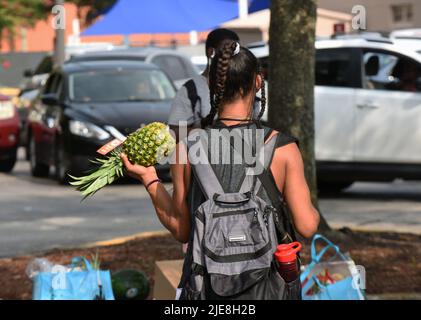 Orlando, Usa. 25.. Juni 2022. Eine Frau trägt eine Ananas, die sie bei einer Lebensmittelverteilungsveranstaltung für Bedürftige erhielt, die von der Second Harvest Food Bank of Central Florida und Orange County in der St. John Vianney Church in Orlando, Florida, gesponsert wird. Hohe Lebensmittel- und Gaspreise drücken die arbeitenden Familien unter Druck und schicken einige zum ersten Mal in Lebensmittelvorratskammern, aber die Anbieter kämpfen mit den Inflationskosten, da die Nachfrage steigt. Kredit: SOPA Images Limited/Alamy Live Nachrichten Stockfoto