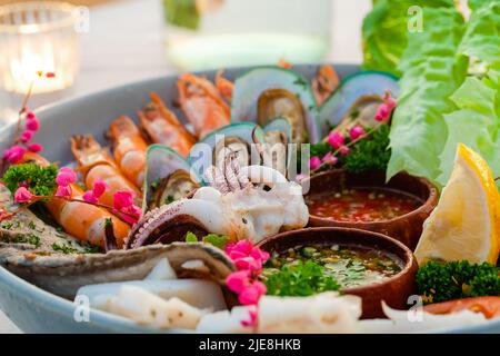 Seafood-Teller im Luxusrestaurant. Abendessen mit gekochten Garnelen, Tintenfisch, Muscheln und Fischsaucen. Tisch mit frischen Meeresfrüchten Platte mit Garnelen Stockfoto