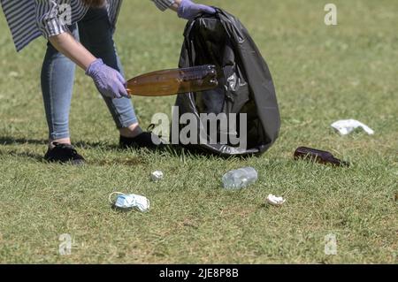 Eine Frau sammelt Plastikmüll in einem Beutel, Abfall, der im Wald auf dem Gras verstreut ist. Stockfoto