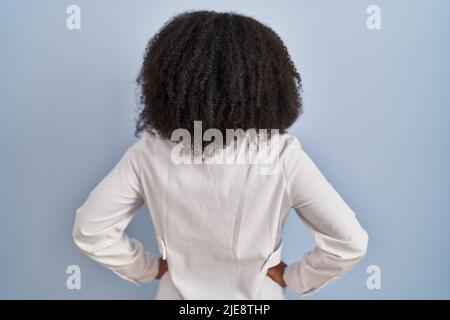 Junge afroamerikanische Frau trägt Arzt Uniform und Stethoskop stehen Rückwärts und mit den Armen am Körper wegschauen Stockfoto