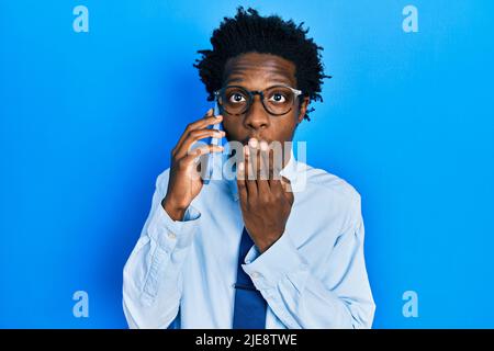 Junger afroamerikanischer Mann mit Gespräch Gespräch auf dem Smartphone über den Mund mit der Hand, schockiert und Angst vor Fehler. Überrascht expressio Stockfoto