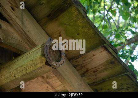Ein altes, abgenutztes und rostetes Metallhufeisen wurde an die hellgraue Holztür eines Dorfhauses genagelt. Hufeisen ist ein Zeichen von Glück und Glück. Stockfoto