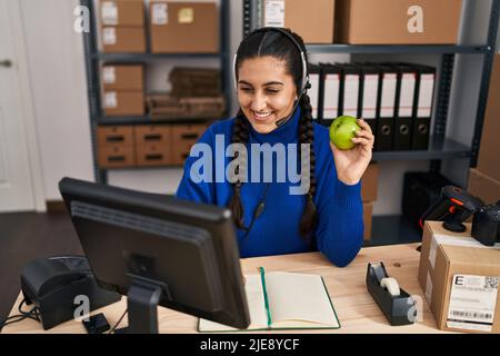 Junge hispanische Frau E-Commerce Call Center Agent mit Videoanruf halten Apfel im Büro Stockfoto