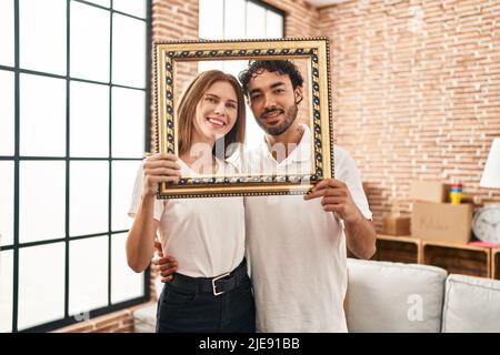 Zwei junge Menschen halten einen leeren Rahmen zusammen und lächeln mit einem fröhlichen und kühlen Lächeln im Gesicht. Sie zeigen Zähne. Stockfoto
