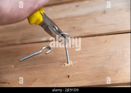 Der Vorgang, bei dem eine Halbringschraube in eine Platine geschraubt wird. Die Hand des Mannes schraubt die C-förmigen Schrauben in die gebohrten Löcher. Nahaufnahme. Selektiver Fokus. Stockfoto