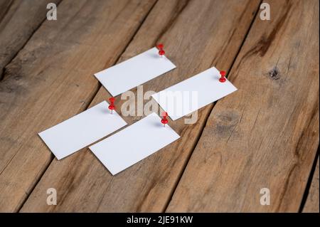 Leere Visitenkarten vor einem hölzernen Hintergrund. Vier Rechtecke aus weißem Papier, die mit Stecknadeln an alten Brettern befestigt sind. Selektiver Fokus. Stockfoto