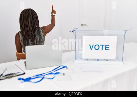 Die junge afroamerikanische Frau, die bei den politischen Wahlen arbeitet, posiert mit der Hand rückwärts und zeigt nach vorne Stockfoto