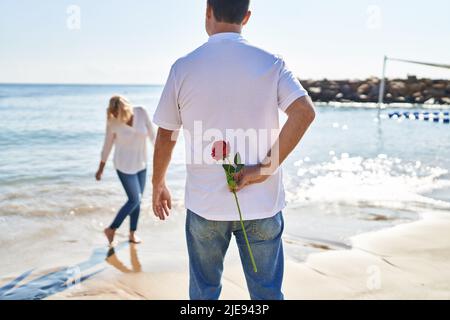 Mann und Frau im mittleren Alter überraschen am Meer mit Blumen auf dem Rücken Stockfoto