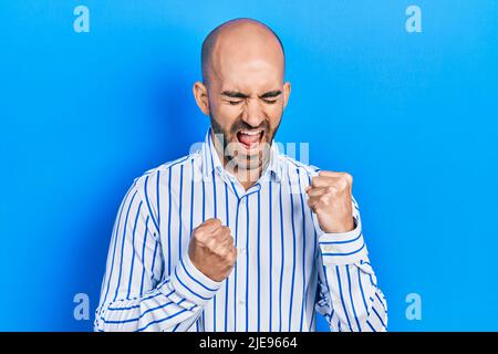 Junger kahlköpfiger Mann in eleganten Kleidern, der überrascht und erstaunt über den Erfolg mit erhobenen Armen und geschlossenen Augen zelebriert Stockfoto