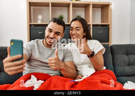 Junges lateinamerikanisches krankes Paar, das zu Hause eine medizinische Fernsultation mit dem Smartphone hat. Stockfoto