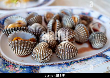 Selektiver Fokus, gekochte oder gekochte Herzmuschel auf dem geschlagenen Gericht und Meeresfrüchte-Gewürzsauce auf der Seite servieren. Stockfoto