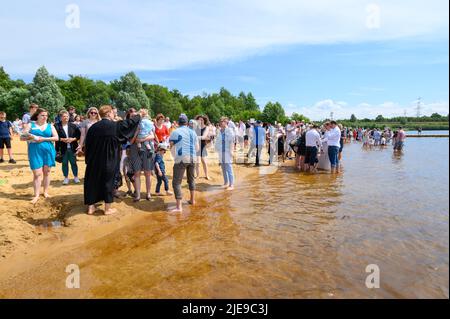 Norderstedt, Deutschland. 26.. Juni 2022. Zahlreiche Getaufte stehen mit Pastoren und ihren Familien am Ufer des Stadtparksee. Eine Massentaufe mit 57 Teilnehmern und rund 500 Gästen wurde von sieben Kirchengemeinden am und im Stadtparksee in Norderstedt bei Hamburg gefeiert. Quelle: Jonas Walzberg/dpa/Alamy Live News Stockfoto