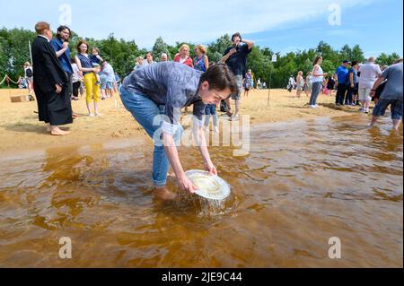 Norderstedt, Deutschland. 26.. Juni 2022. Pate Lukas holt vor der Taufe Wasser aus dem Stadtparksee für sein Patenkind. Sieben Kirchengemeinden am und im Stadtparksee in Norderstedt bei Hamburg feierten eine Massentaufe mit 57 Teilnehmern und rund 500 Gästen. Quelle: Jonas Walzberg/dpa/Alamy Live News Stockfoto