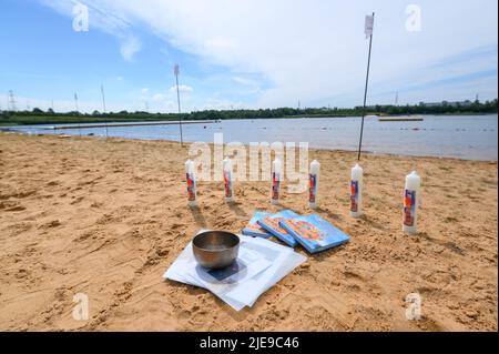 Norderstedt, Deutschland. 26.. Juni 2022. Taufkerzen, Bücher und eine Metallschale stehen vor der Taufe am Strand am Ufer des Stadtparksee. Eine Massentaufe mit 57 Teilnehmern und rund 500 Gästen wurde von sieben Kirchengemeinden am und im Stadtparksee in Norderstedt bei Hamburg gefeiert. Quelle: Jonas Walzberg/dpa/Alamy Live News Stockfoto