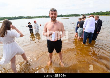 Norderstedt, Deutschland. 26.. Juni 2022. Getauft Mirko Hein (49), steht nach seiner Taufe mit einer Taufkerze im Stadtparksee. Sieben Kirchengemeinden am und im Stadtparksee in Norderstedt bei Hamburg feierten eine Massentaufe mit 57 Teilnehmern und rund 500 Gästen. Quelle: Jonas Walzberg/dpa/Alamy Live News Stockfoto