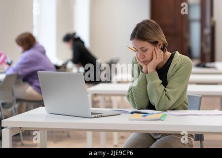 Verärgert weibliche reife Studentin, die in der Bibliothek an schwierigen Hausaufgaben arbeitet, müde vom Studium Stockfoto