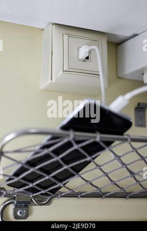 Ein Smartphone lädt in einem Abteilwagen eines Personenzuges über eine spezielle Steckdose Stockfoto