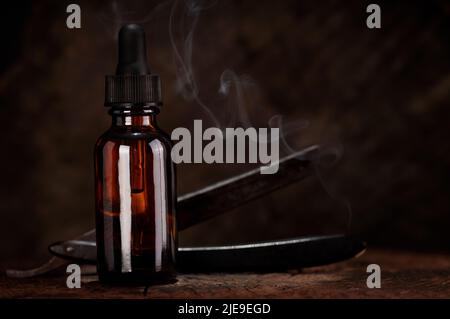 Bartpflege-Konzept, Flasche mit Dropper alten Rasiermesser in Nahaufnahme auf dunklem Holzhintergrund Barber Shop Werkzeuge auf Holzhintergrund plus Rauch. Stockfoto