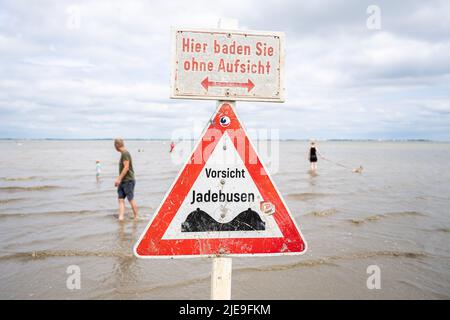 Dangast, Deutschland. 26.. Juni 2022. Am Nordseestrand von Dangast befindet sich ein Schild mit der Aufschrift 'Hier schwimmt man ohne Aufsicht - Vorsicht Jade Bay', während einige Leute im Wasser sind. Kredit: Mohssen Assanimoghaddam/dpa/Alamy Live Nachrichten Stockfoto