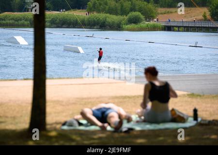 Norderstedt, Deutschland. 26.. Juni 2022. Ein Wasserskifahrer ist auf dem Stadtparksee unterwegs, während Tagesausflügler die Sonne am Ufer genießen. Quelle: Jonas Walzberg/dpa/Alamy Live News Stockfoto