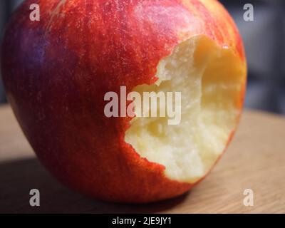 Ein gebissenen roten Apfel auf einer hölzernen Oberfläche. Makro „Reifer Apfel“. Stockfoto