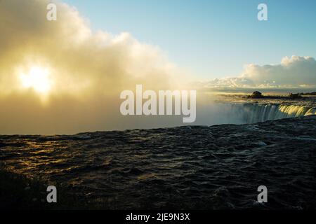 Die Sonne scheint durch den Nebel und die Wassersprühnebel der Canadian Falls oder Horseshoe Falls von Niagara am frühen Morgen Sonnenaufgang auf der kanadischen Seite Stockfoto