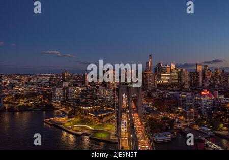 Starker Verkehr auf mehrspuriger Straße auf Brücke. Hohe Wohngebäude im Stadtbezirk. Lichter in der abendlichen Stadtkulisse. Brooklyn, New York City, USA Stockfoto