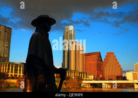 Eine Skulpturenstatue des Rock and Roll-Musikers und Gitarristen Stevie Ray Vaughn steht in Silhouette vor der Skyline von Austin Texas Stockfoto