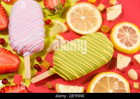 Zwei Eiscremes auf einem Stock - Erdbeere und Zitrone auf gelbem und rotem Hintergrund. Sommerliche Fruchtdesserts Stockfoto