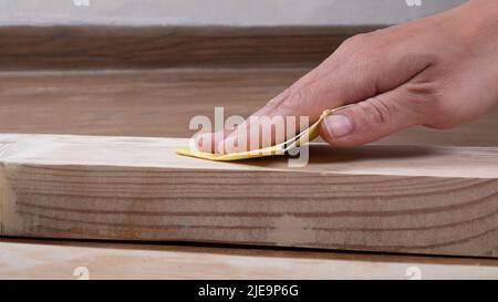 Meister reibt die Tür mit Schleifpapier, Restaurierung von Holzprodukten. Stockfoto