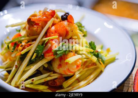 Grüner Mangosalat mit Riesengarnelen auf weißem Teller aus dem Thai Food Restaurant Stockfoto