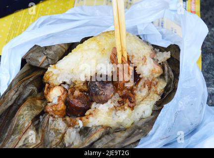 Essstäbchen greifen den berühmten Hong Kong Dim Sum 'Lo Mai Gai' auf, den klebrigen Reis, der von einem Lotusblatt umwickelt ist. Stockfoto