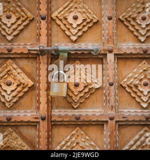 Fragment minimalistischer Holzschnitzereien auf antikem Holztor. Eingangstür aus Vintage-Holz mit Vorhängeschloss Stockfoto