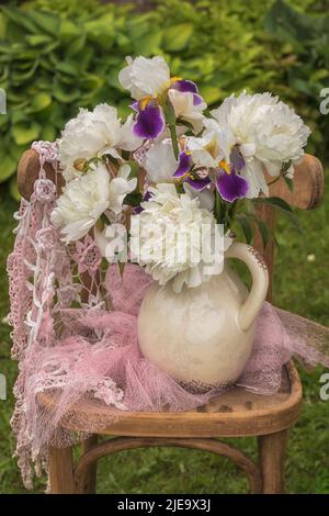 Bouquet von bärtigen Iris und weißen Pfingstrosen auf einem Stuhl. Stockfoto