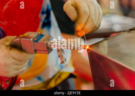 Nahaufnahme: Schweißer Hände mit Handlaserschweißmaschine Stockfoto