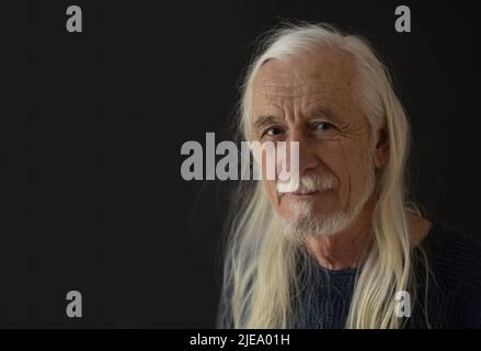 Low-Key-Studio-Porträt von lächelndem attraktiven alten Mann mit losen langen grauen Haaren. Horizontal. Stockfoto