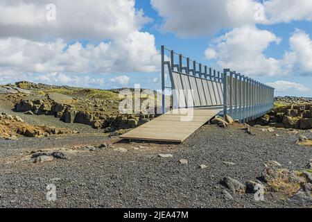 Brücke in Island auf der Halbinsel Reykjanes. Brücke führt über die nordamerikanischen und eurasischen Spalten. Lava Felsen im Hintergrund und Wolken im Stockfoto