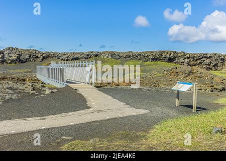 Weg zu einer Metallbrücke auf der isländischen Halbinsel Reykjanes. Landschaft mit Lavagesteinen über die nordamerikanischen und eurasischen Spalten. Grünes Gras mit Grau Stockfoto