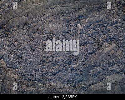 Lavafeld von oben. Abgekühlter Lavastrom mit Strukturen in dunkler Farbe. Muster von abgelenkten und gebrochenen Felsen aus geflasener Lava. Verschiedene Grautöne Stockfoto