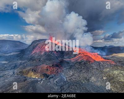 Aktiver Vulkan mit einem kleinen Brunnen aus dem Krater. Vulkan mit flüssigem Magma auf der isländischen Halbinsel Reykjanes. Grüne, rotgraue und dunkle Lavagesteine Stockfoto