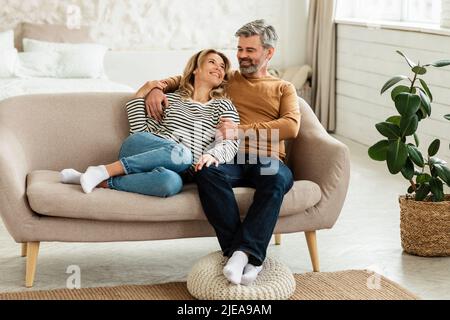 Glückliches Paar Mittleren Alters, Das Sich Auf Dem Sofa Zu Hause Umarmte Stockfoto